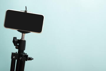 Smartphone on a tripod on a light blue background. The desktop of a modern blogger with a place for text