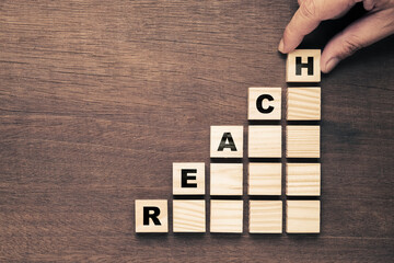 Hand arranges the wood blocks with REACH word stack up on the step stairs to the top level, online...