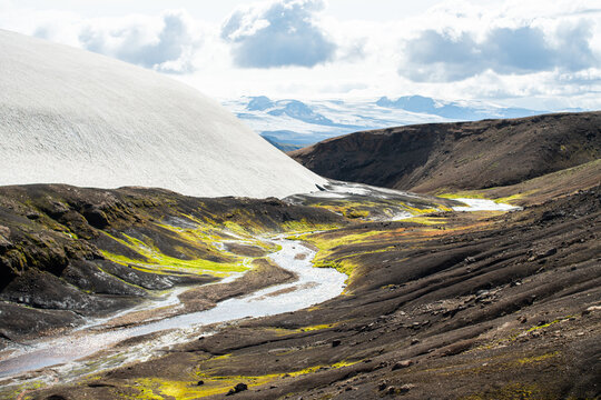 Snowy mountain next to small river creek surrounded bij green moss, Iceland