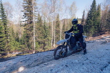 Fototapeta na wymiar Rider riding dirt motorcycle on snowy off-road on summer day in mountains