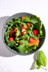 Plate with fresh salad of arugula, plants, cheese, basil and strawberry.