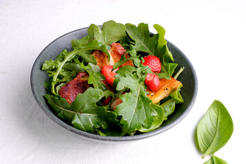 Plate with fresh salad of arugula, plants, cheese, basil and strawberry.