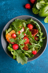 Plate with fresh salad of arugula, plants, cheese, basil and strawberry.