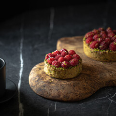 Two delicious raspberry tartlets with pistachios on a gray background