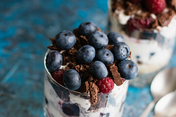 Delicious dessert with blueberries, yogurt, chocolate and oatmeal, close-up, in a glass cup. Berries close-up in a glass with dessert