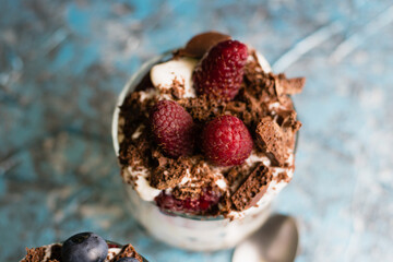 Delicious dessert with raspberries, yogurt, chocolate and oatmeal, close-up, in a glass cup. Berries close-up in a glass with dessert