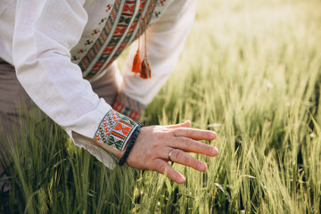 A man in Ukrainian embroidery touches wheat at sunset. Concept of preservation of Ukrainian grain,...