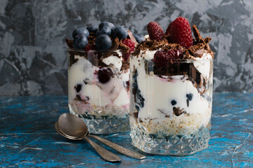 Delicious desserts with raspberries, yogurt, blueberries, cherries, chocolate and oatmeal on a dark background