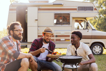 A group of friends spend time together in nature. Middle-aged men prepare a barbecue near an RV