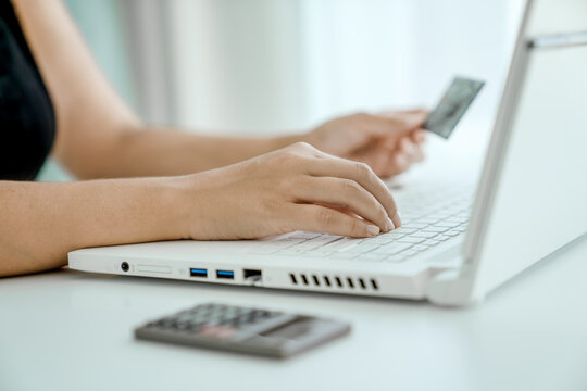 Woman makes online purchases sitting in front of laptop with bank card in her hand. Hands close-up. Concept of online shopping and money transfer.