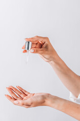Hands of cropped white woman holding cosmetic serum pipette