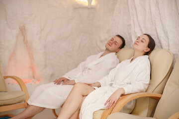 Young man and woman in a white bathrobes relaxing in a salt room