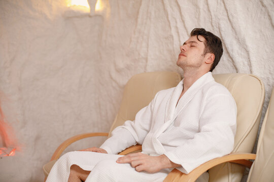 Young man in a white bathrobe relaxing in a salt room and sleeping