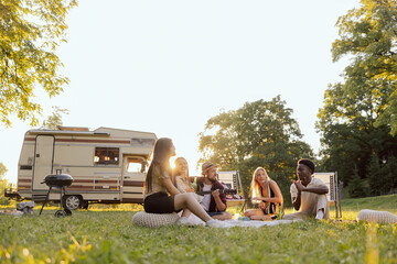 A group of college friends spend time together traveling in a camper van. A bearded middle-aged boy plays guitar.