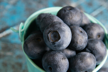 Blueberry berry in a small decorative bucket on a blue concrete background macro