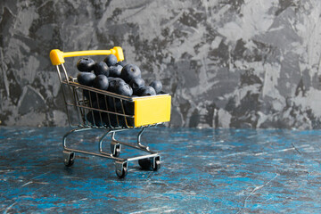 Blueberry berry in a decorative shopping cart on a dark background with copy space. Concept of...