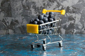 Blueberry berry in a decorative shopping cart on a dark background with copy space. Concept of...