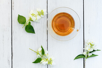 Jasmine tea in glass cup and flowers on a wooden white background ,view from above. Cup with green...