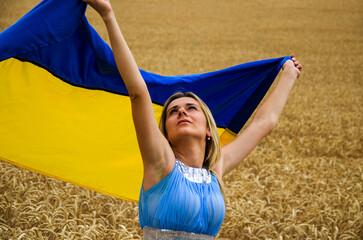 Girl with the Ukrainian flag. A girl with a blue and yellow flag in a wheat field. Ukrainian wheat fields. Harvesting during the war. War in Ukraine. Arson of Ukrainian fields.Girl with Ukrainian flag