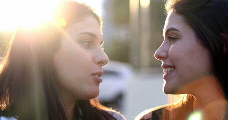 Millennial girlfriends looking at each other with sunshine lens-flare, romantic atmosphere