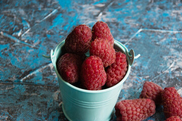 Raspberries in a blue decorative bucket macro on a background with copy space