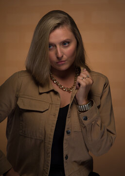 Portrait of a young, beautiful girl with blue eyes and blonde hair in a beige jacket. She looks sternly. She is wearing an expensive watch, a gold chain and rings