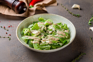 Green vegetable salad with broccoli and greenery with sauce on brown table