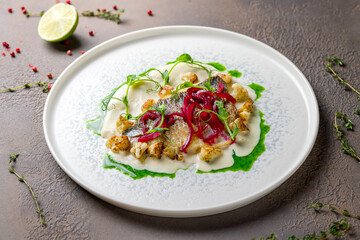 Dorado on grill on plate with sauce and red marinated onion on brown table