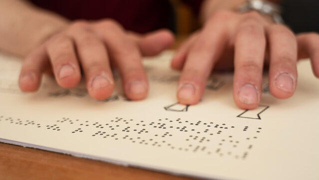 Visually impaired man reading a braille book. 