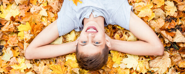 Happy teenager in white t-shirt relax autumn season. lies and smiles at the autumn golden leaves in park. concept calm and peace. Caucasian guy in on fallen wedge leaves sunny day. photo banner