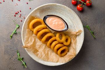 Rings of squid in batter with coctail sauce on brown table top view
