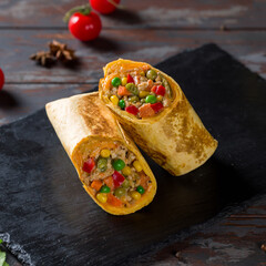 Mexican chicken burrito with spices, vegetables and cheese on black stone plate