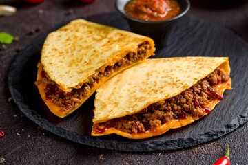 Quesadilla with beef, cheese, bbq sauce and sauces on dark stone plate macro close up