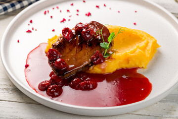 Duck breast with berry sauce and mashed potatoes on white plate on white wooden table macro close up