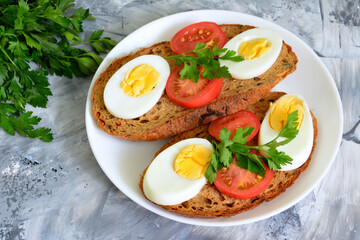 bread slices with boiled eggs and tomatoes on plate decorated with parsley, close-up