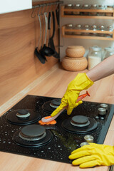 a woman washes the hob in the kitchen, hands in yellow rubber gloves clean the stove