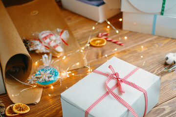 Christmas gift, gingerbread, sweets, craft wrapping paper and garlands on wooden table. Festive mood and holiday decorations. Surprise for New Year.