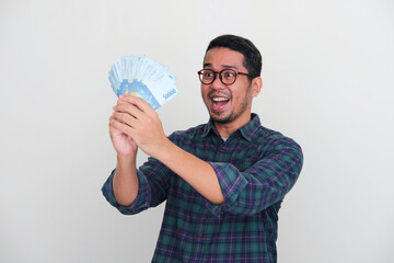 Adult Asian man looking to money that he hold with cheerful expression