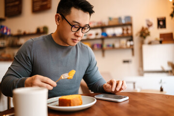 Adult asian man using cellphone while having breakfast in cafe indoors