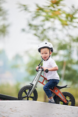 Portrait of child riding balance bike. Male toddler kid in helmet learning to ride on run bicycle at skate park.