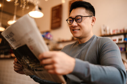 Adult Asian Man Reading Newspaper While Resting In Cafe Indoors