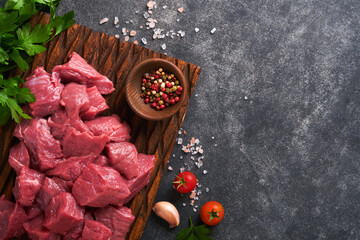 Raw chopped beef meat. Raw organic meat beef or lamb, spices, herbs on old wooden board on dark grey concrete background. Goulash. Raw uncooked meat. Meat with blood. Top view with copy space.