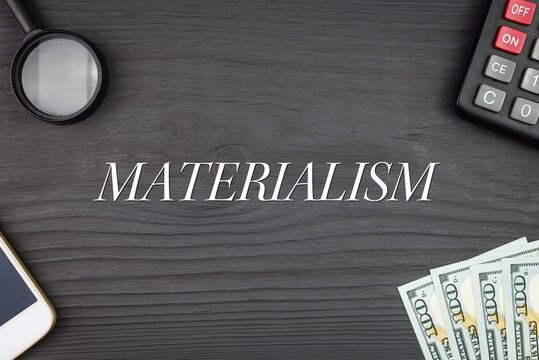 MATERIALISM - word (text) and money dollars on the table, phone magnifying glass (loupe) and calculator. Business concept, buying goods and products, paying for services (copy space).