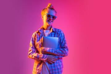 Portrait of adorable young girl wearing plaid shirt isolated on magenta color background in neon light. Concept of beauty, art, fashion, emotions