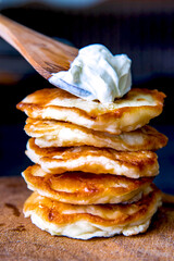 Fritters on a wooden board with sour cream. Pancakes