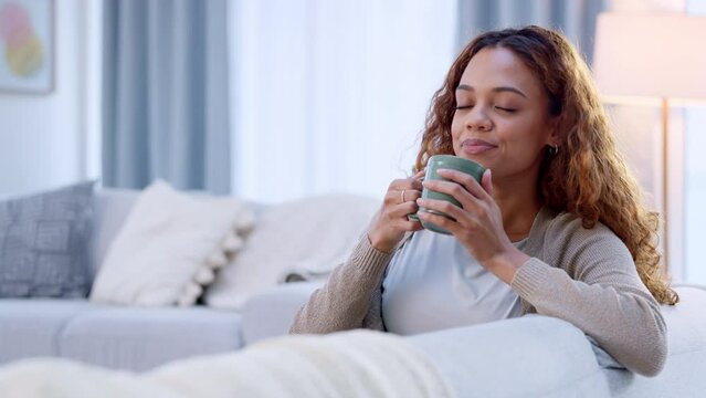 Relaxed woman drinking coffee and feeling carefree and refreshed while relaxing on the couch at home. Female taking deep breath and smelling the aroma of a hot beverage, feeling mindful and content