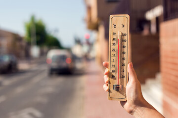 Hot weather. Thermometer in front of an urban scene during heatwave. - obrazy, fototapety, plakaty