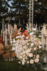 The decor of the wedding photo zone is in the open air. There are bouquets of white flowers on the lawn, tall candles in glass candlesticks, and dry hydrangeas.