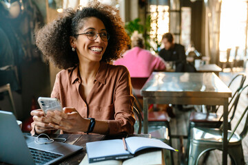 Young african american woman using cellphone while working in cafe