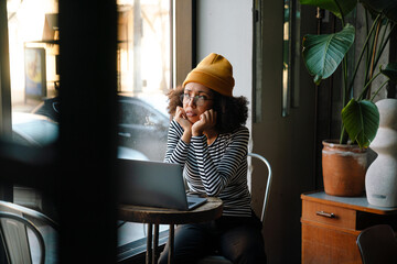 Young african woman looking through window while sitting in cafe